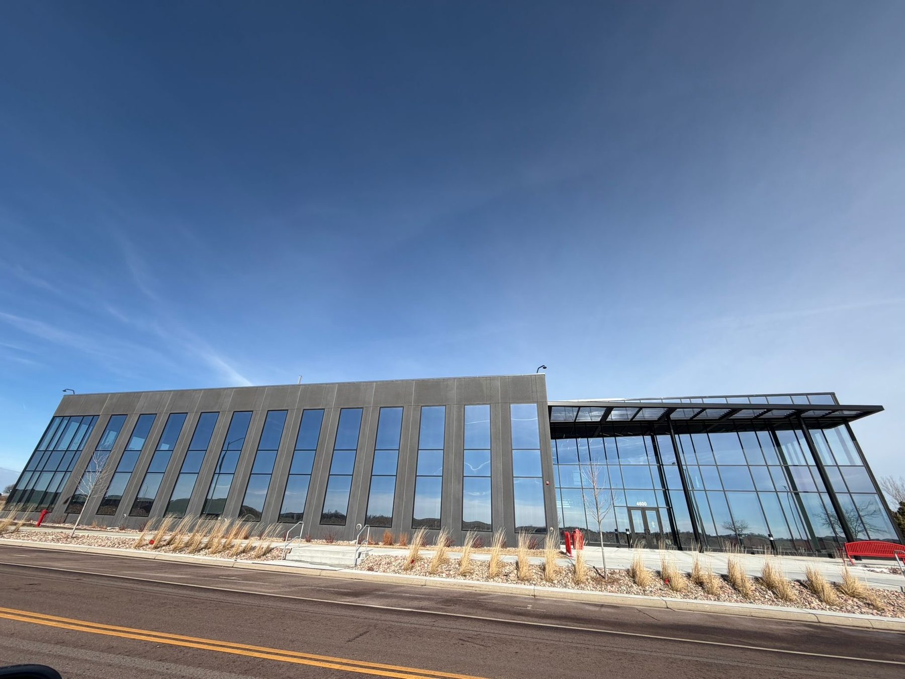 The Discovery District building at 4800 North Career Avenue, a long two storey building in dark precast concrete with tall narrow windows and a glazed entrance, photographed from the road under a clear blue sky.